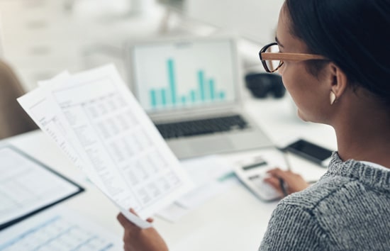 Femme qui examine des documents financiers à son bureau Femme qui examine des documents financiers à son bureau